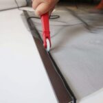 Hand using red twin-wheel spline roller tool to install spline along a flyscreen frame edge