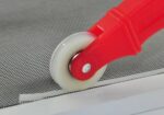 Nylon wheel of red spline roller tool pressing rubber spline into a flyscreen frame channel over mesh