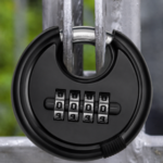 Black 70mm combination disc padlock locked through a galvanised steel gate, showing the shrouded hardened shackle