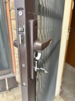 Brown hinged security screen door lock installed, inside lever, snib turn and key with mortice latch and deadbolt visible