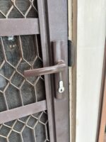 Brown hinged security screen door lock installed on a brown security door, outside lever handle and keyed cylinder