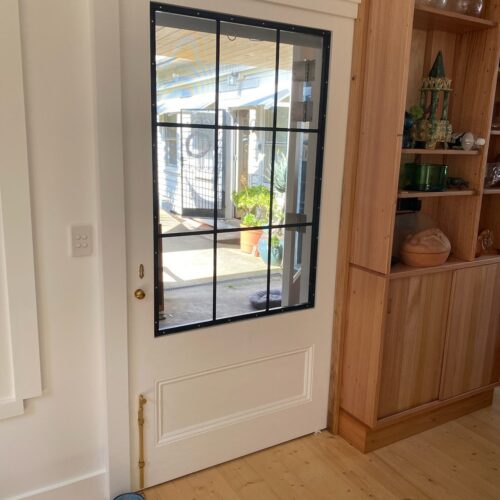 TradeBase 316 marine grade stainless steel flyscreen mesh installed in a white timber screen door with black steel glazing bars, exterior view