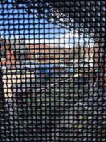 Looking out through black 316 stainless steel security mesh from inside a house to a street, cars and sky clearly visible